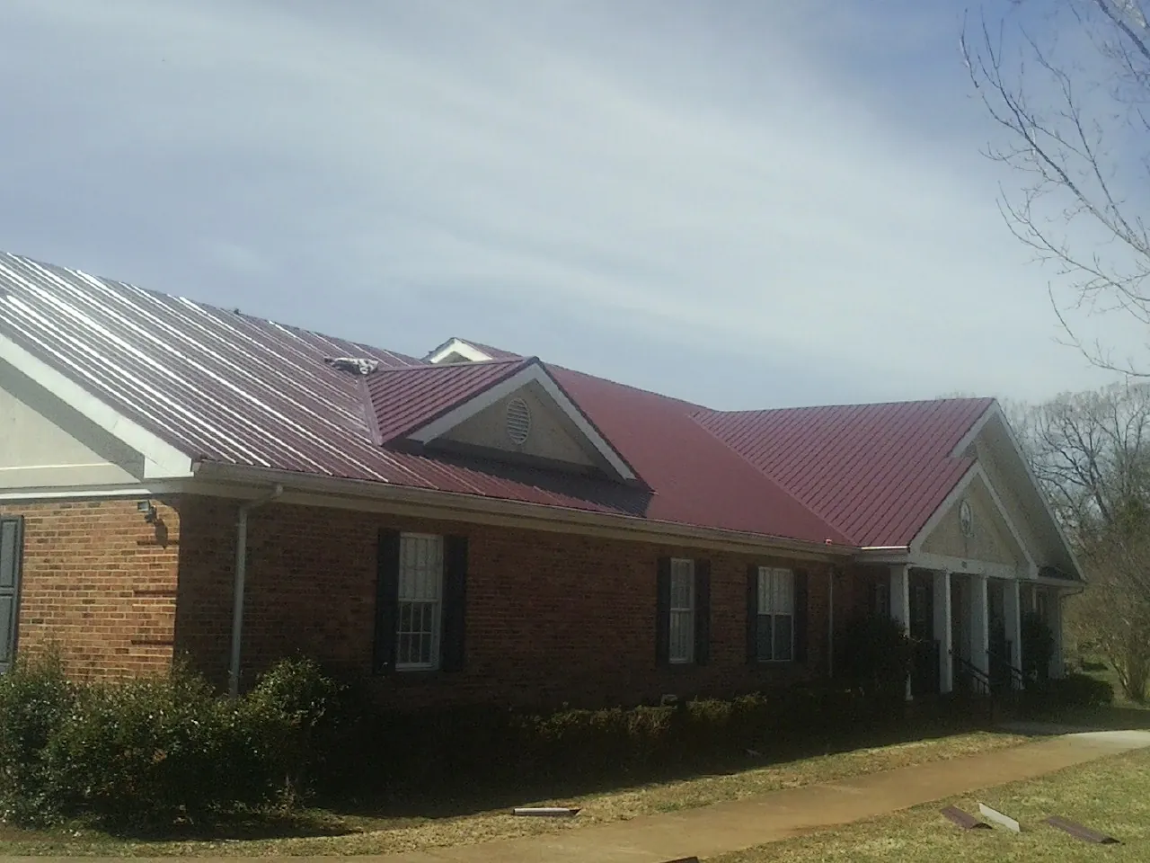 Red metal roof with gabled entries on a long brick building, from a Hail Damage Roof Repair job in Martinsville